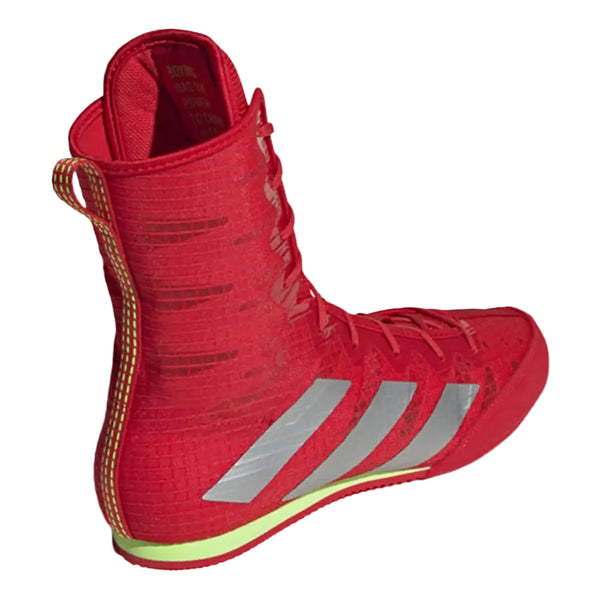 A red high-top boxing shoe by Adidas, shown from a side profile view against a light gray background. The shoe features three silver stripes on the side, a textured knit upper, a gold-colored pull loop, and a neon yellow-green outsole.